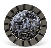 A ceramic plate by Pablo Picasso featuring a black and white painted rustic landscape with houses, foliage, and clouds, surrounded by a dark rim with vertical brushstroke patterns.