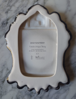 Grayson Perry ceramic artwork with AI-generated image of a doll-like figure in yellow dress, surrounded by cats and symbols, in ornate black ceramic frame reading 