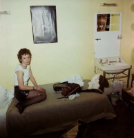Nan Goldin Nan as a punk self-portrait seated on bed in messy room with BOY poster above, wearing punk outfit, digital pigment print