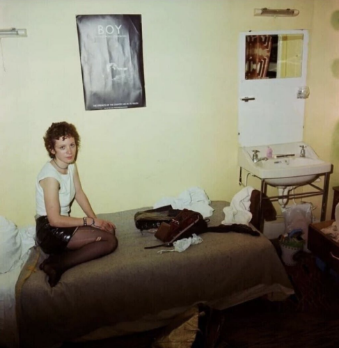 Nan Goldin Nan as a punk self-portrait seated on bed in messy room with BOY poster above, wearing punk outfit, digital pigment print